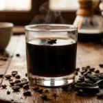 Gelatina negra de café en vaso transparente con granos de café alrededor sobre mesa de madera